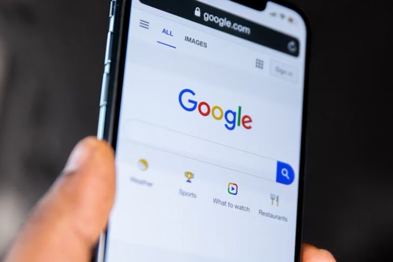 A hand holding a smartphone with the browser open at the Google homepage.