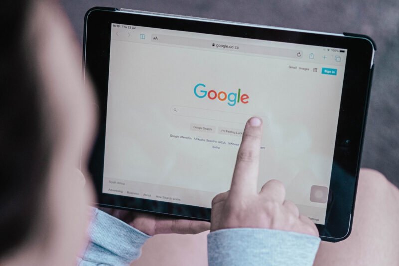 A person pointing to a tablet displaying the Google homepage.
