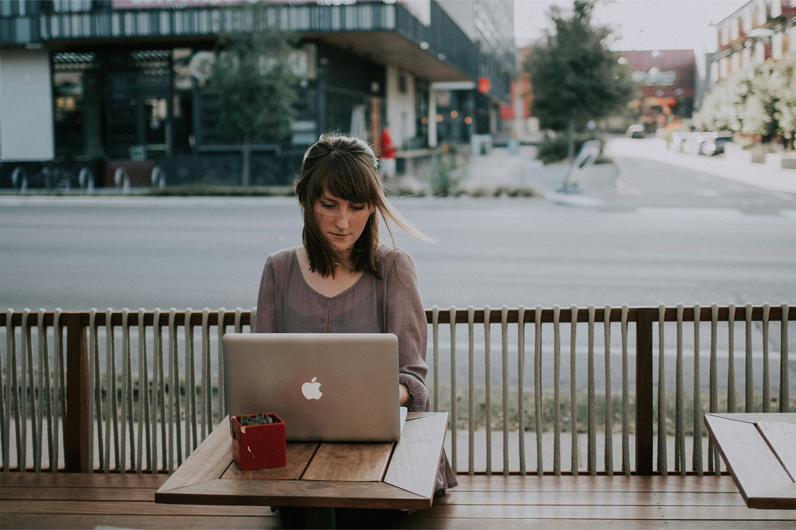 Junge Frau sitzt mit ihrem Laptop in einem Café im Freien.